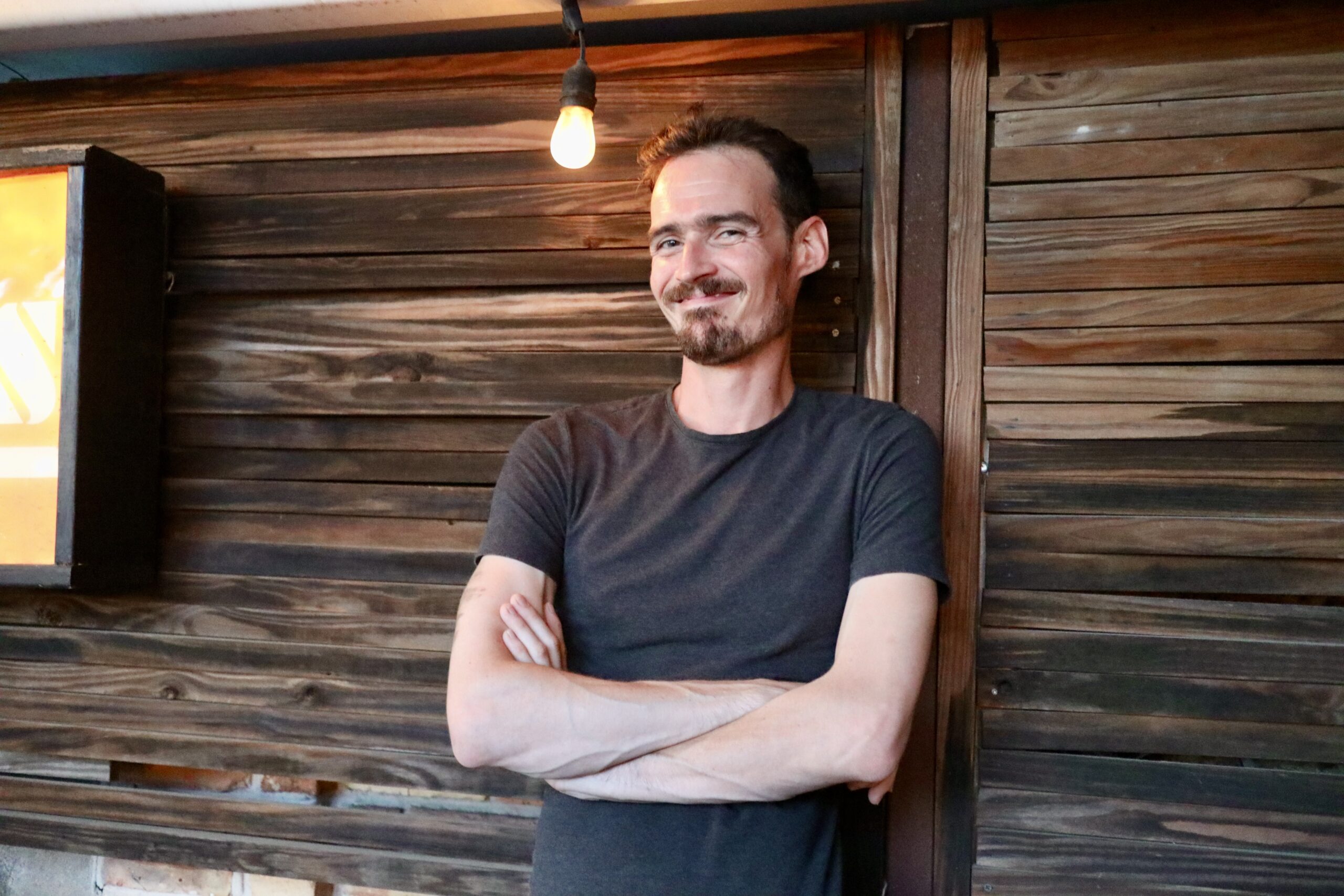 Jean-Marc Buytaert, founder of JMB Creative Solutions, standing against a wooden background with a lightbulb overhead.