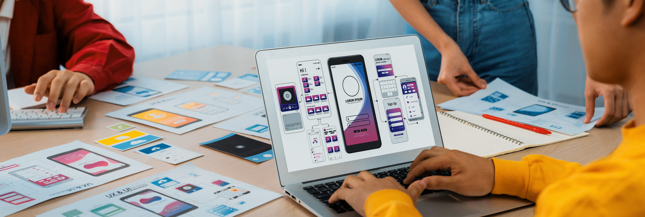 Team working on mobile app design and development with wireframes and prototypes on a laptop and printed layouts.